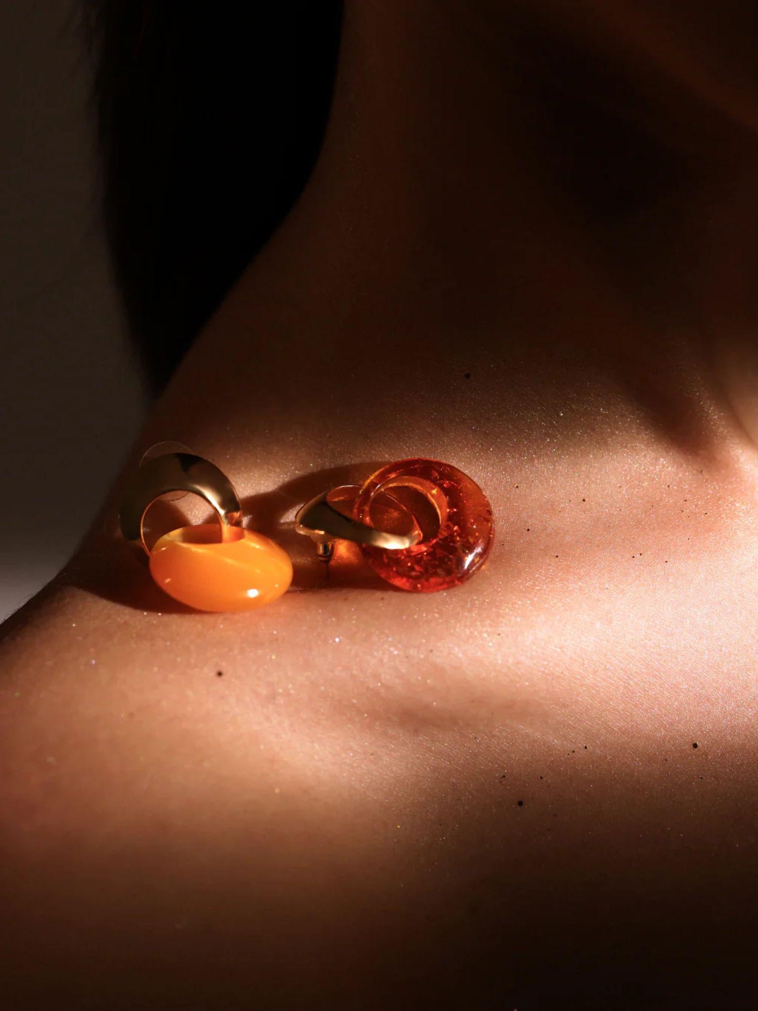 Gold amber hoop earring resting on model's collarbone in warm directional light