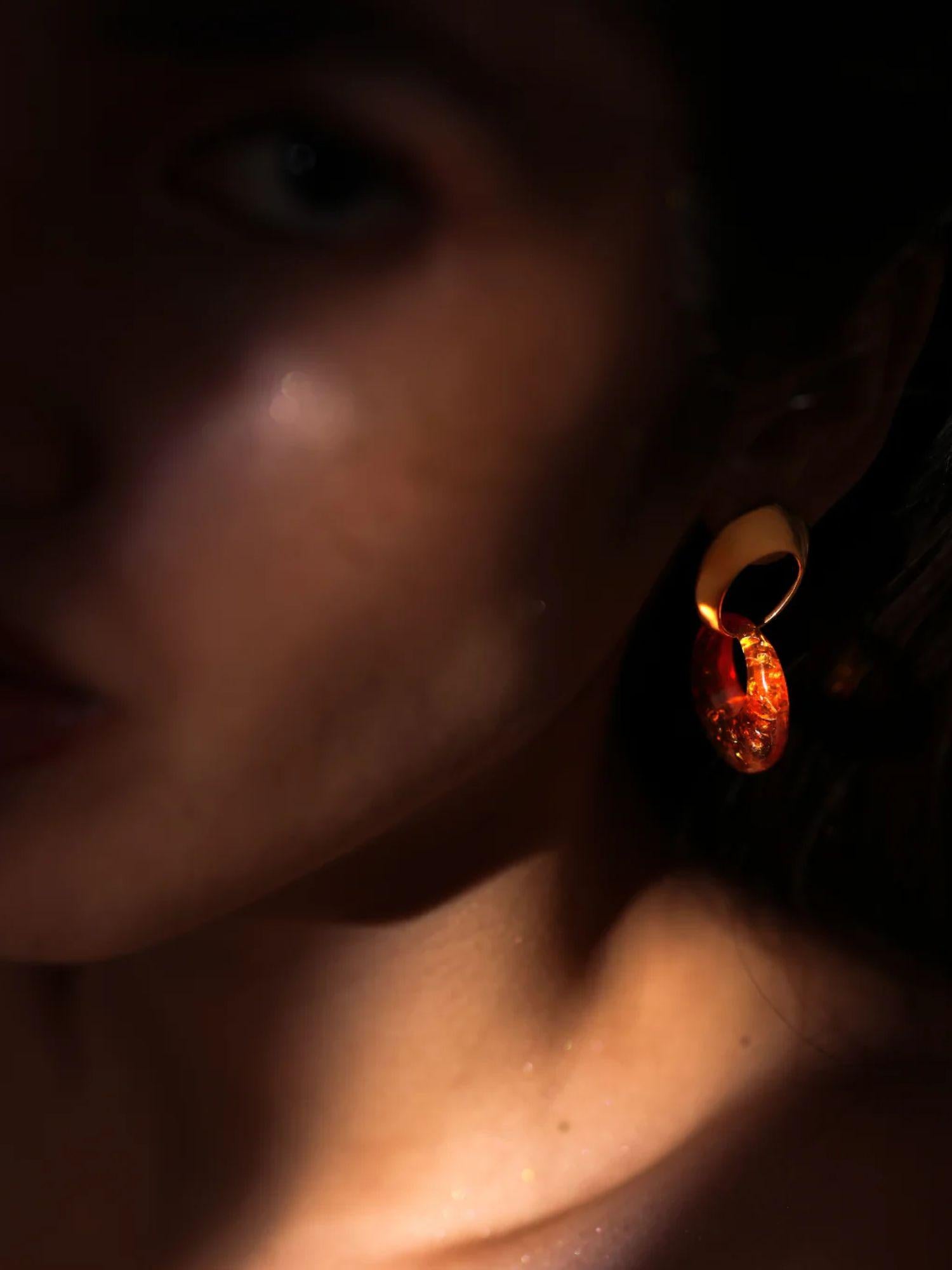 Close-up of gold and lab-grown amber hoop earring on model's ear in warm light
