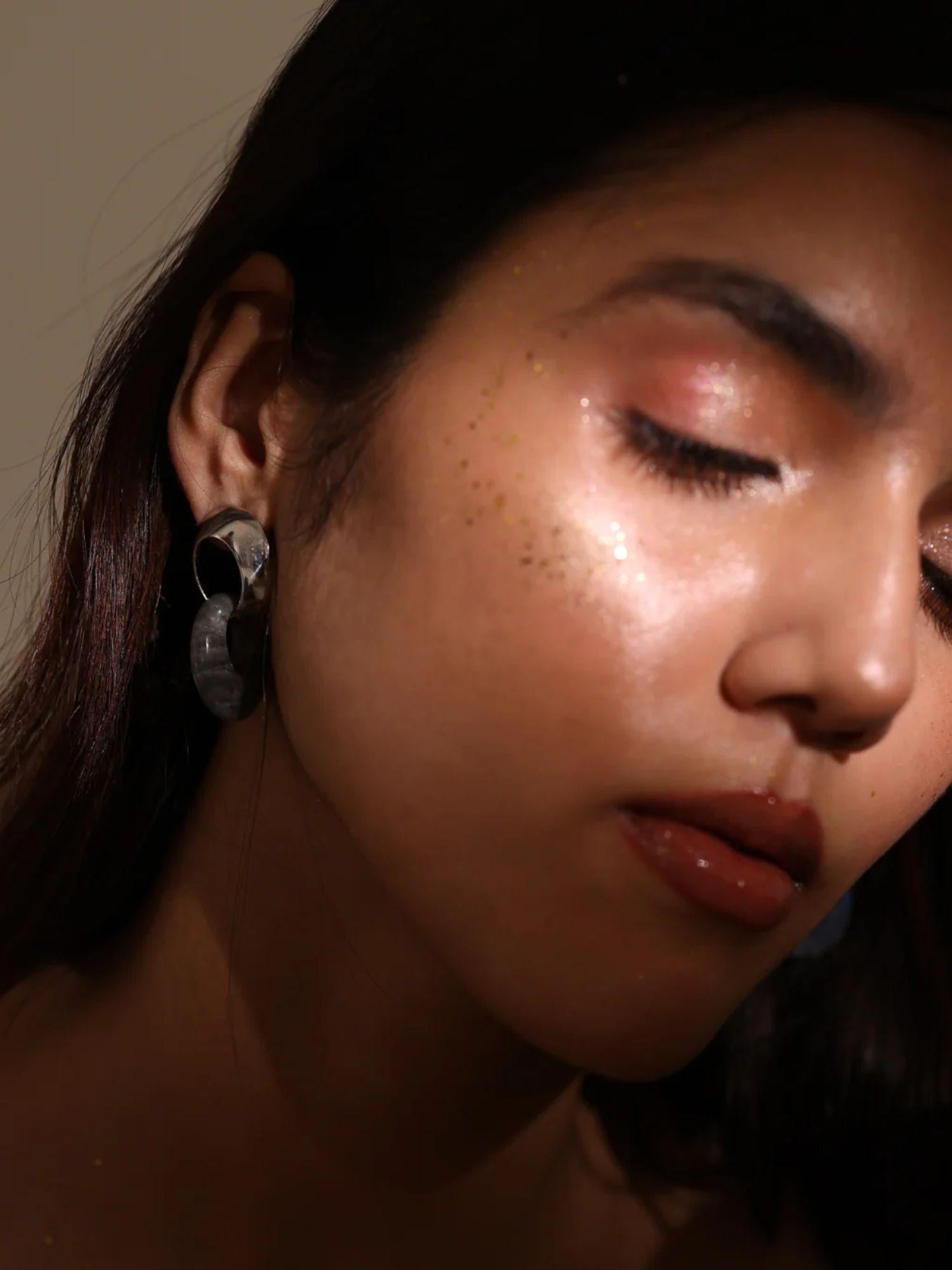 Model with eyes closed wearing gold amber hoop earrings, soft warm light on face