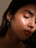 Model with eyes closed wearing gold amber hoop earrings, soft warm light on face