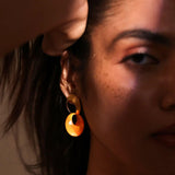 Model wearing gold amber hoop earrings, face partially in shadow, dramatic light