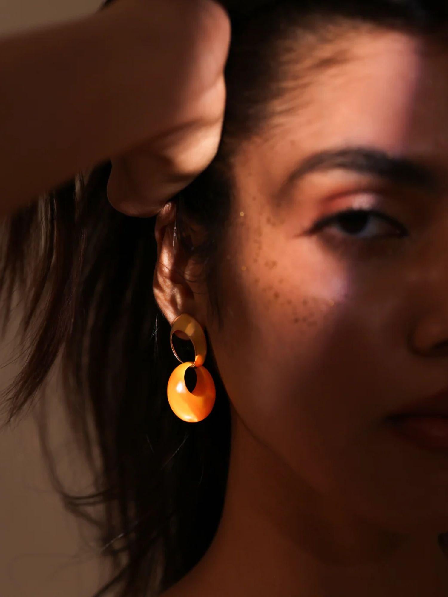Model wearing gold amber hoop earrings, face partially in shadow, dramatic light