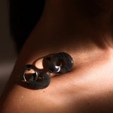 Dark amber double-hoop earring on model's collarbone in dramatic warm light