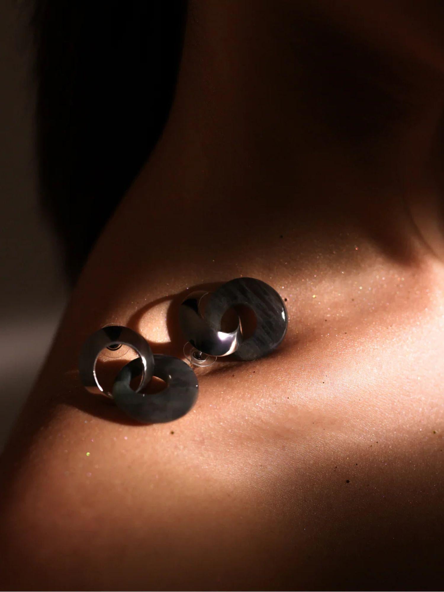 Dark amber double-hoop earring on model's collarbone in dramatic warm light