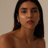 Model in neutral light wearing silver and amber mismatched hoop earrings, front portrait