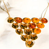 Triangular gold statement necklace with lab-grown amber stones on white marble surface