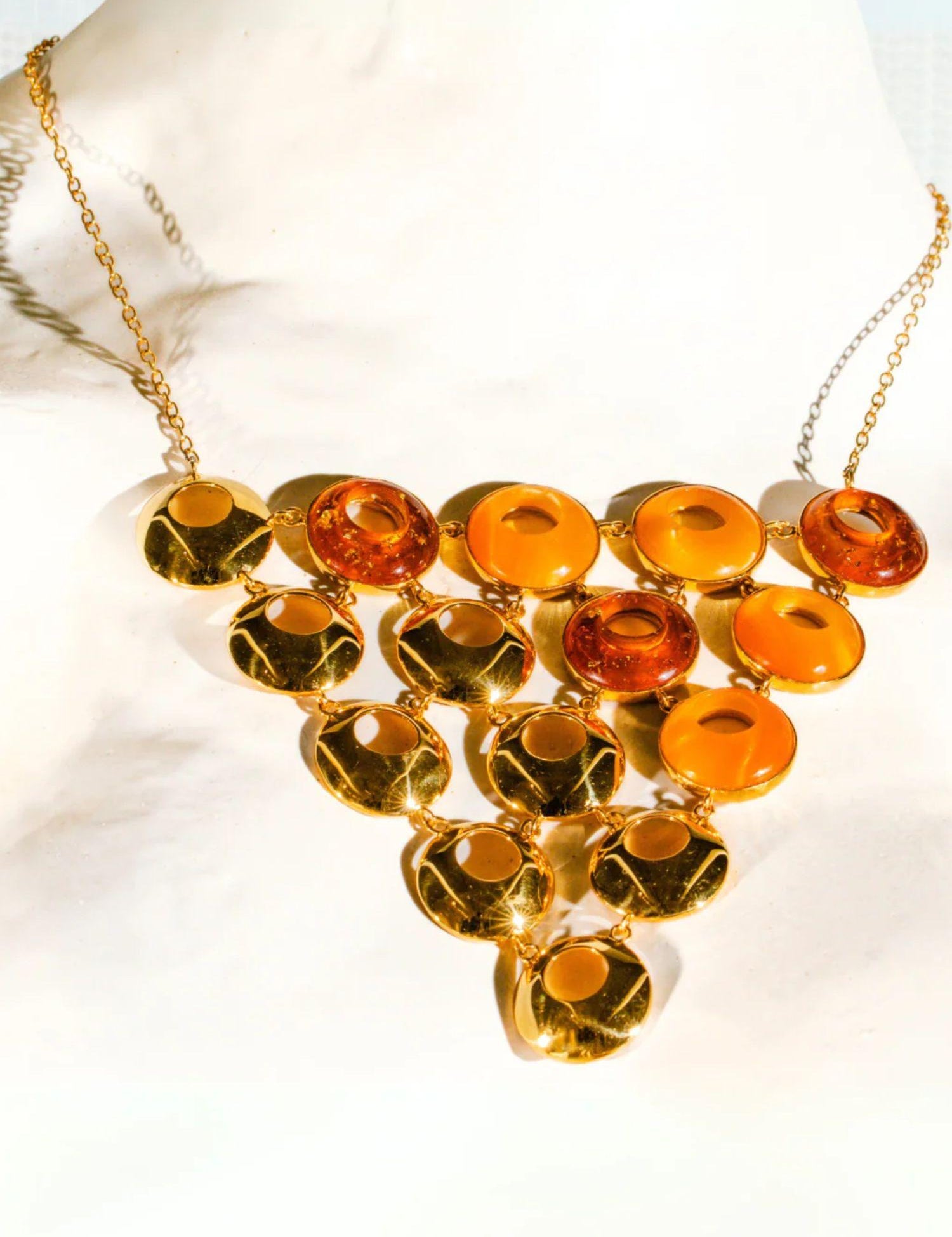 Triangular gold statement necklace with lab-grown amber stones on white marble surface