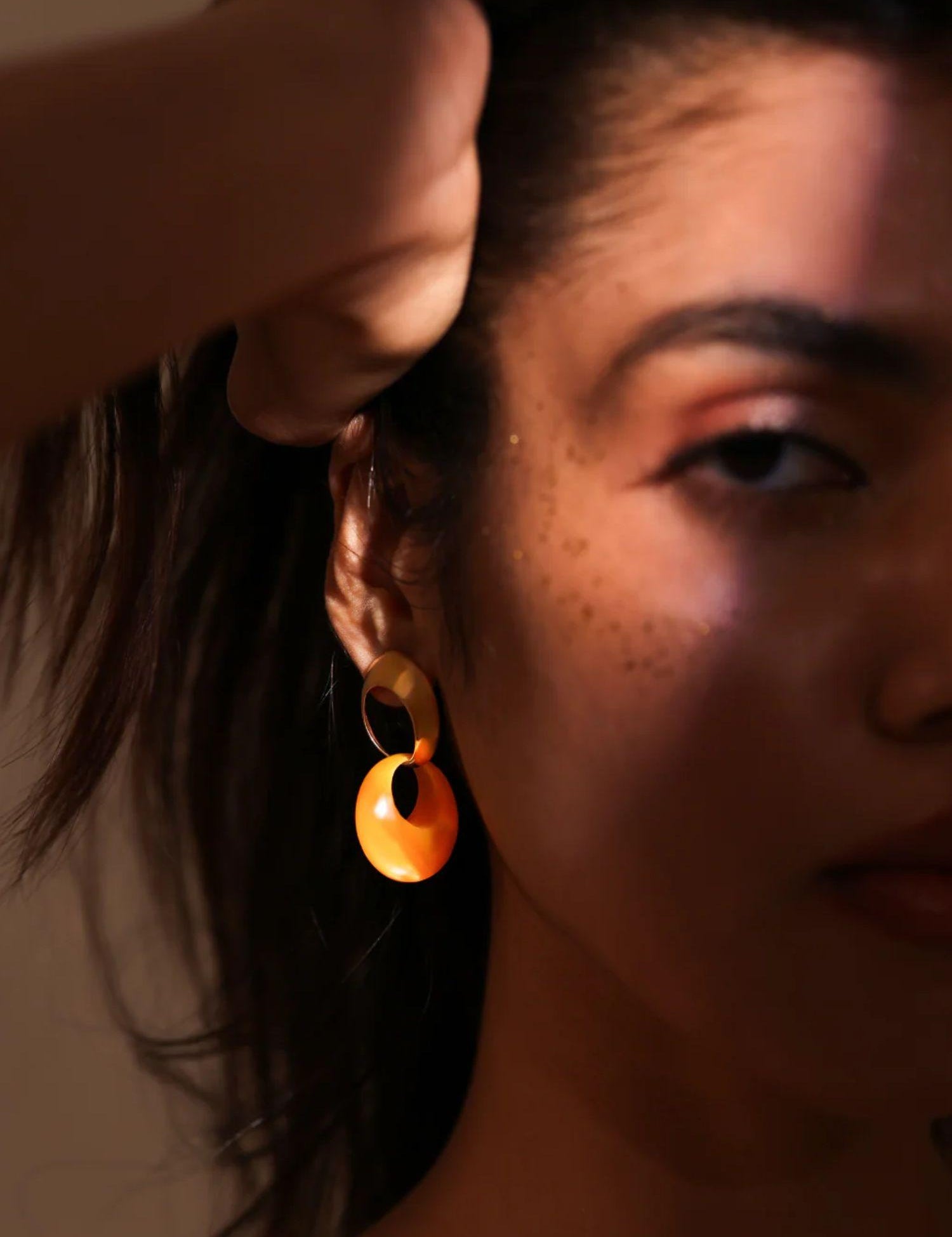 Close-up of model holding gold amber hoop earring near ear in dramatic warm light