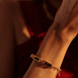 Gold box link bracelet on model's wrist against red fabric in warm light