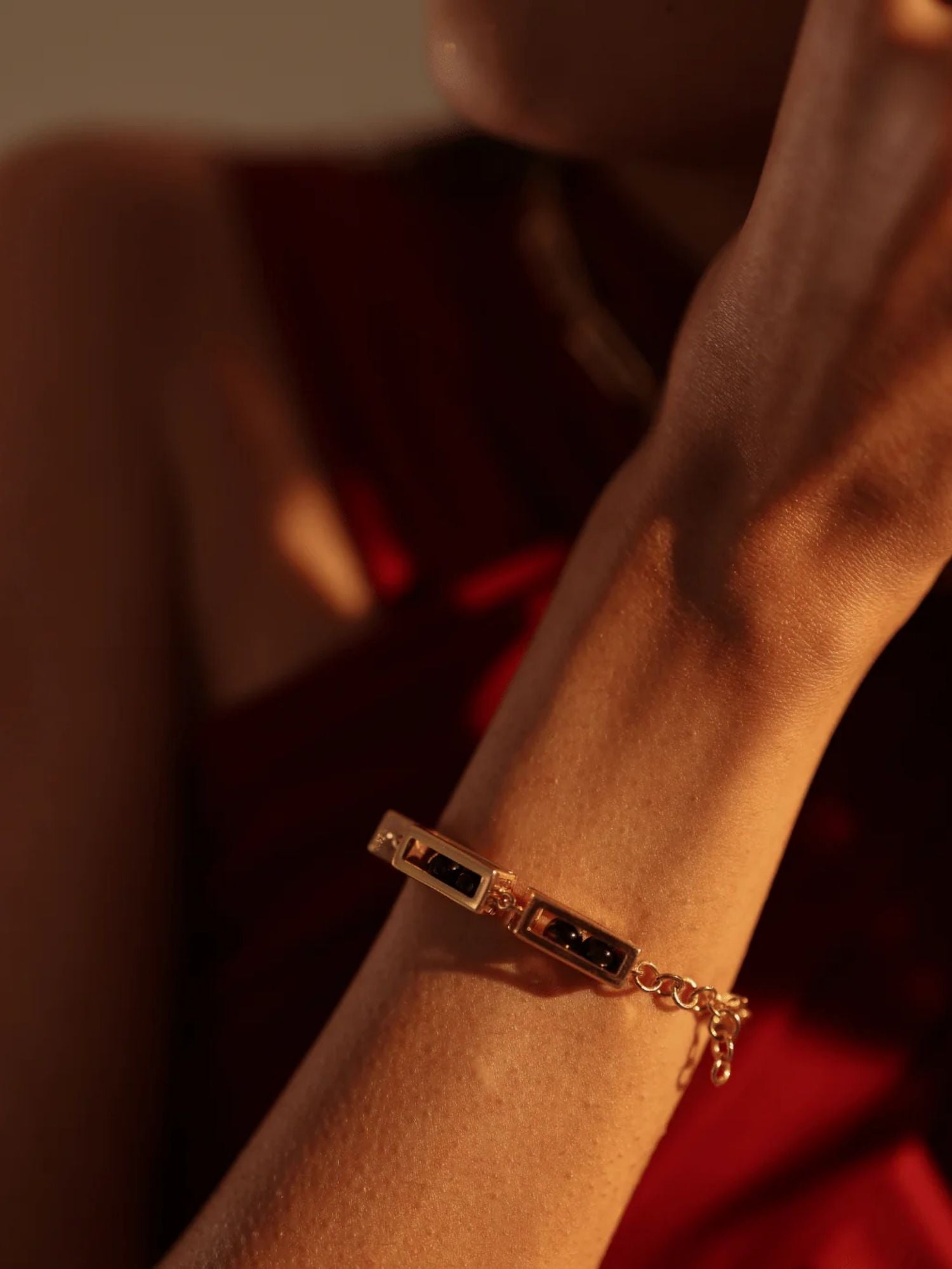 Gold box link bracelet on model's wrist against red fabric in warm light