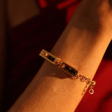 Model wearing gold box link bracelet with agate bead on wrist, warm red light