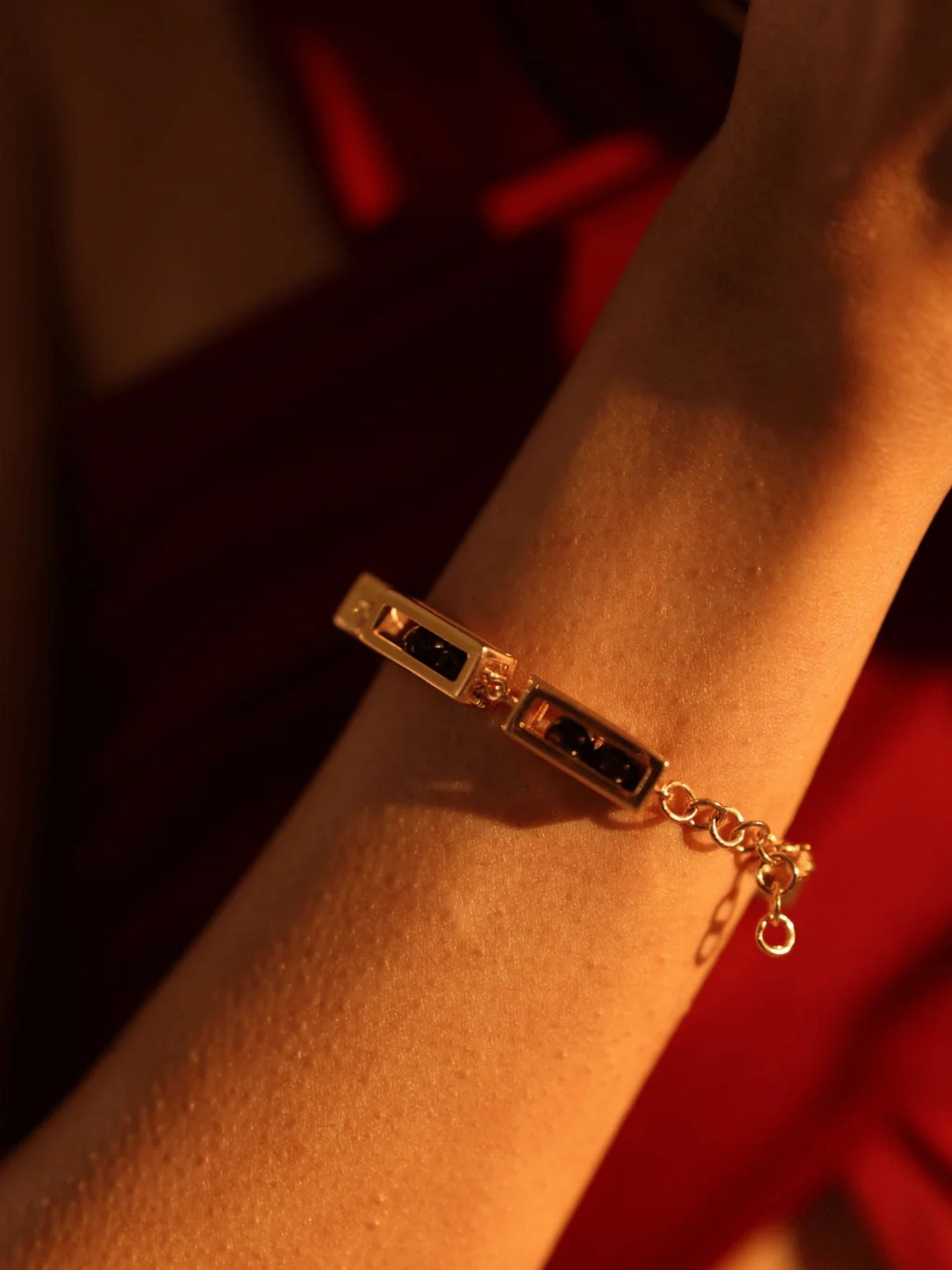 Model wearing gold box link bracelet with agate bead on wrist, warm red light