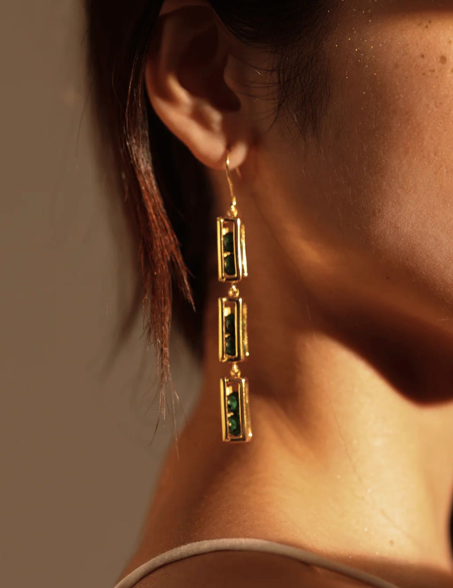 Model wearing long gold box link drop earrings, side profile in warm light