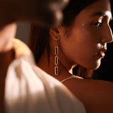 Model in editorial portrait wearing gold triple-drop box link earrings