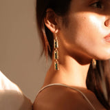 Side profile of model wearing long gold Fill Me In box link earrings in warm light