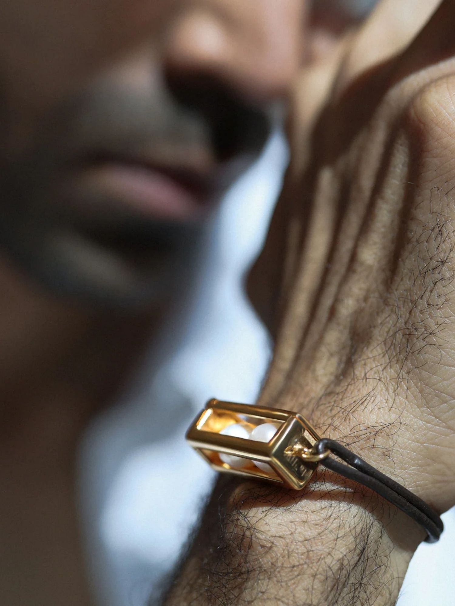 Close-up of male model wearing large gold box leather bracelet, chin in frame
