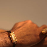 Male model wearing large gold leather cord bracelet on wrist, close-up