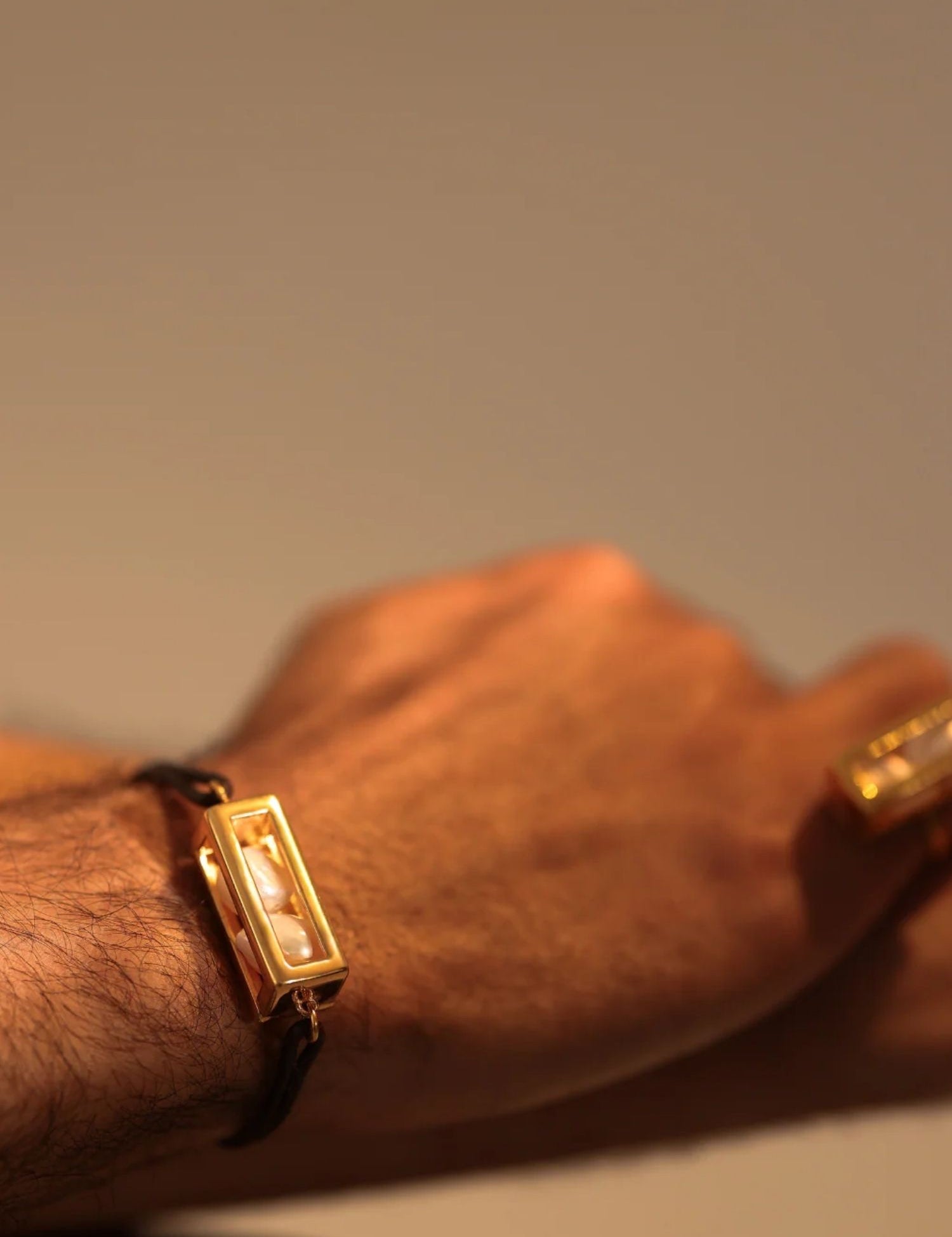 Male model wearing large gold leather cord bracelet on wrist, close-up