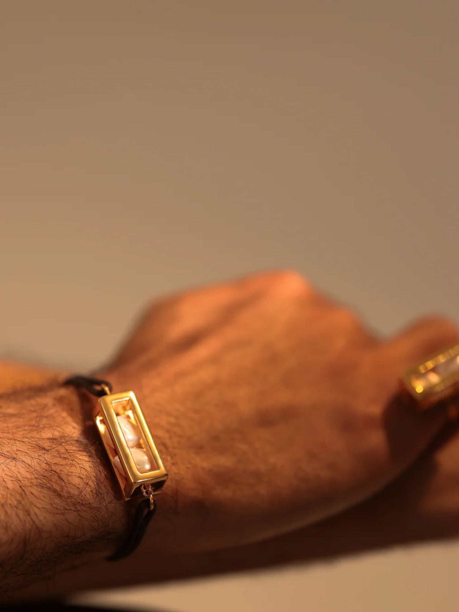 Male model wearing large gold leather cord bracelet on wrist, close-up