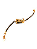 Large gold box motif on dark leather cord bracelet on white background