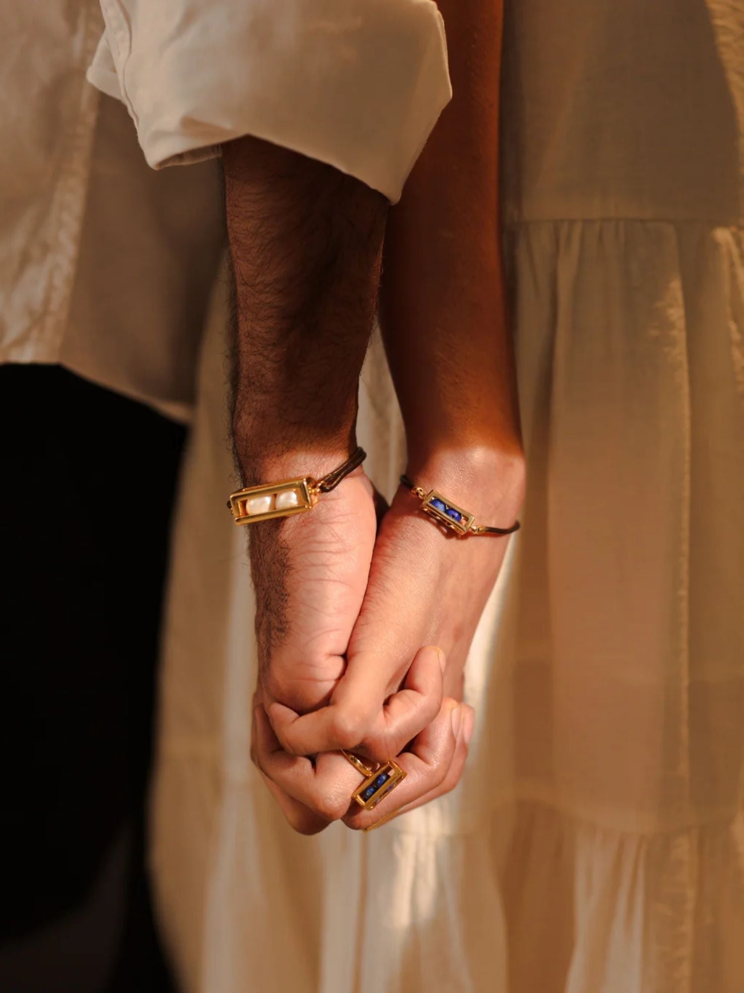 Couple holding hands both wearing gold leather cord Fill Me In bracelets