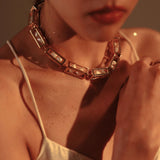 Model in white wearing large gold box link necklace, neck and chin in frame