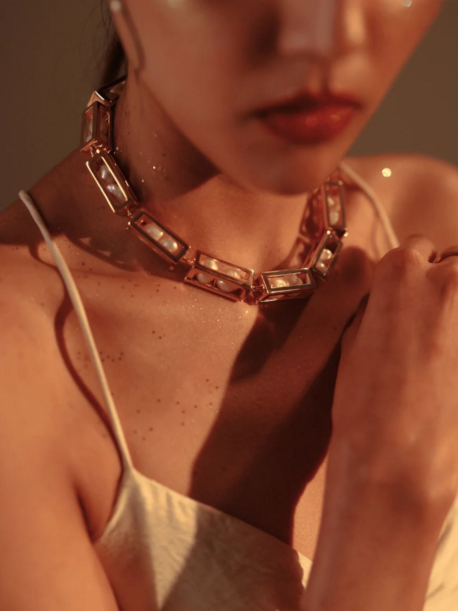 Model in white wearing large gold box link necklace, neck and chin in frame
