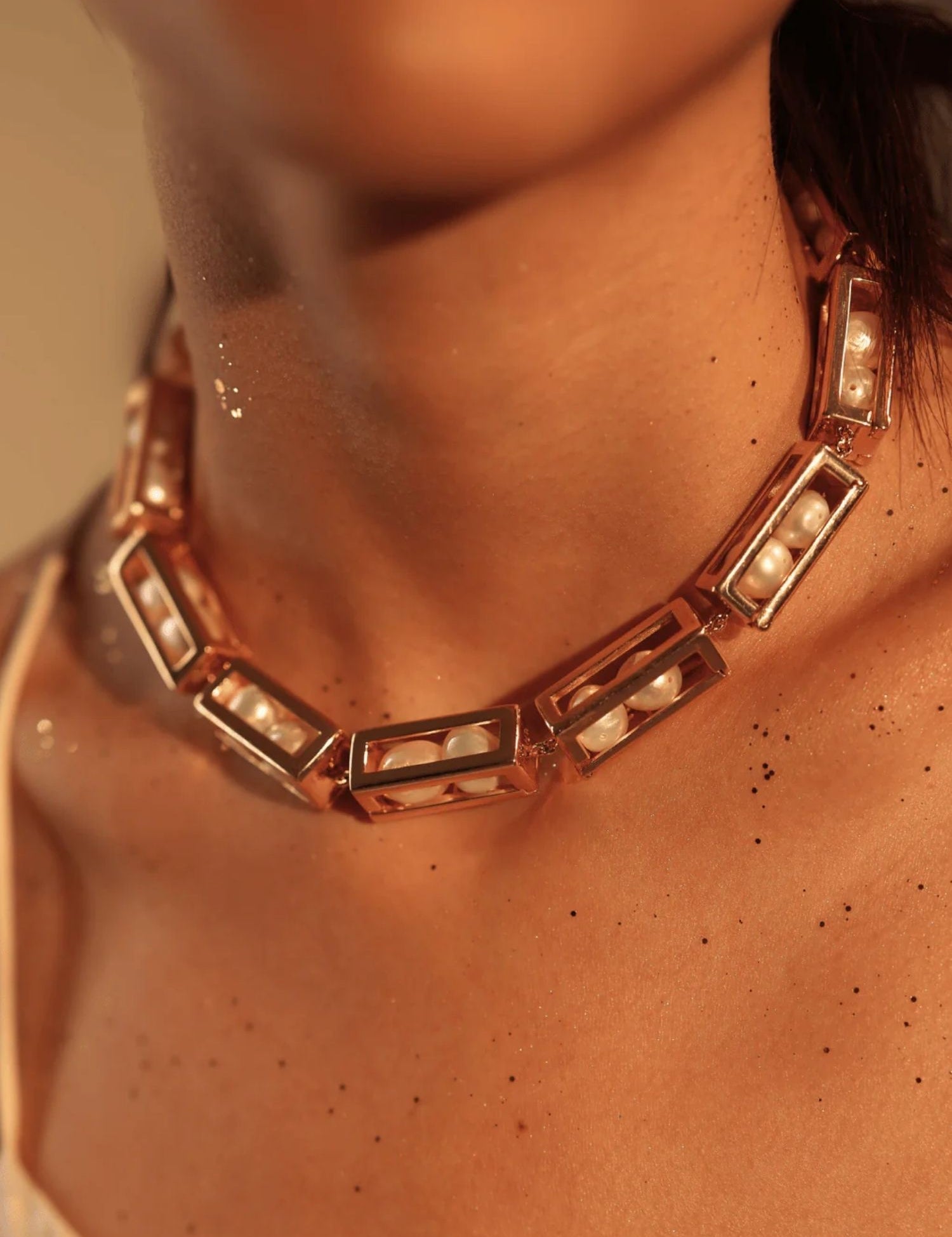 Model wearing large gold box link necklace with pearl beads, collarbone close-up