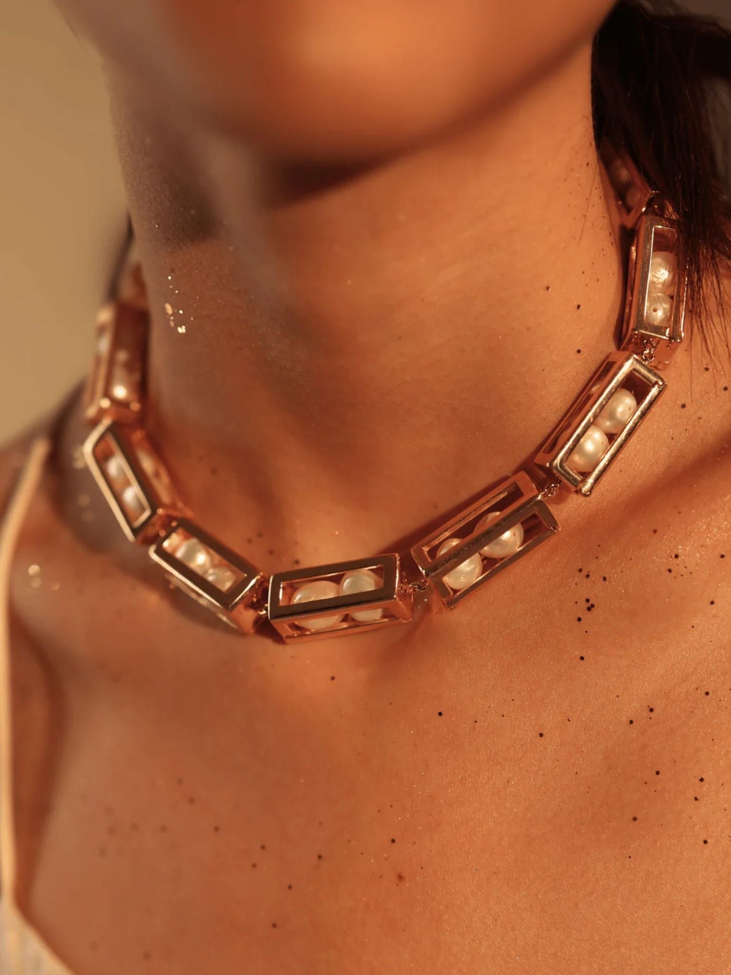 Model wearing large gold box link necklace with pearl beads, collarbone close-up