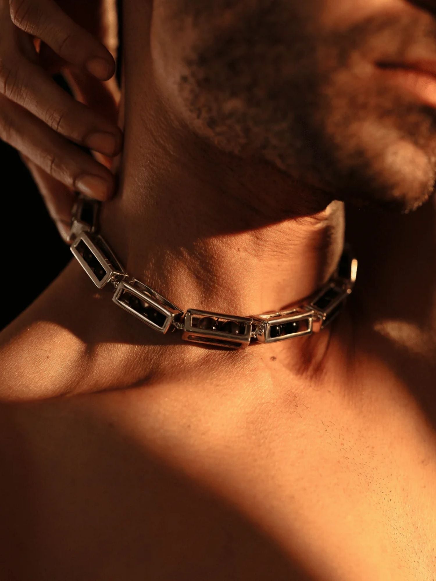 Male model wearing silver box link choker necklace, side profile in warm light