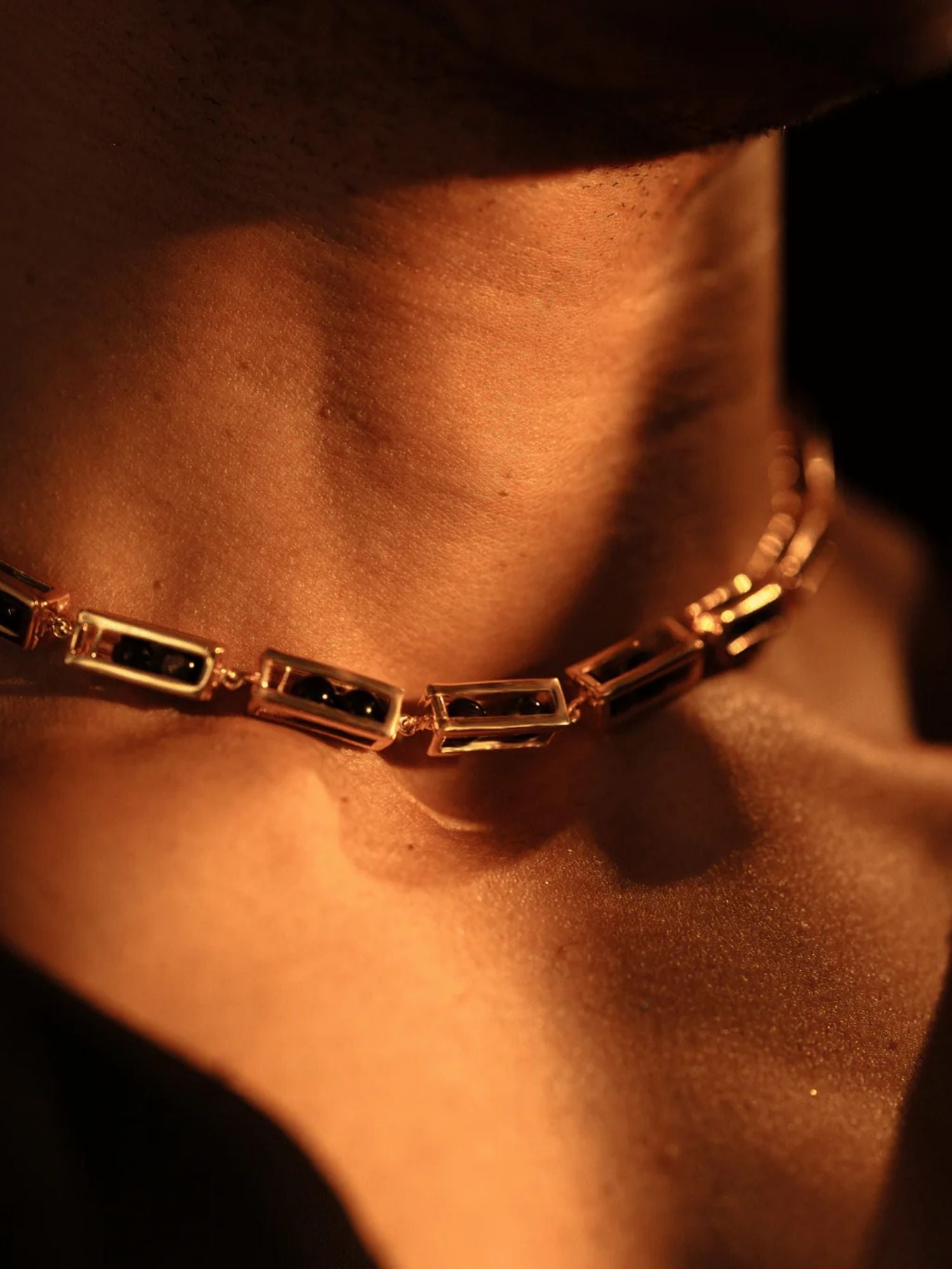 Model wearing gold box link choker necklace with agate beads, collarbone in warm light