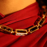 Gold box link necklace on model wearing red, close-up collarbone editorial shot
