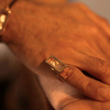 Close-up of large gold interchangeable box ring on model's hand, warm light