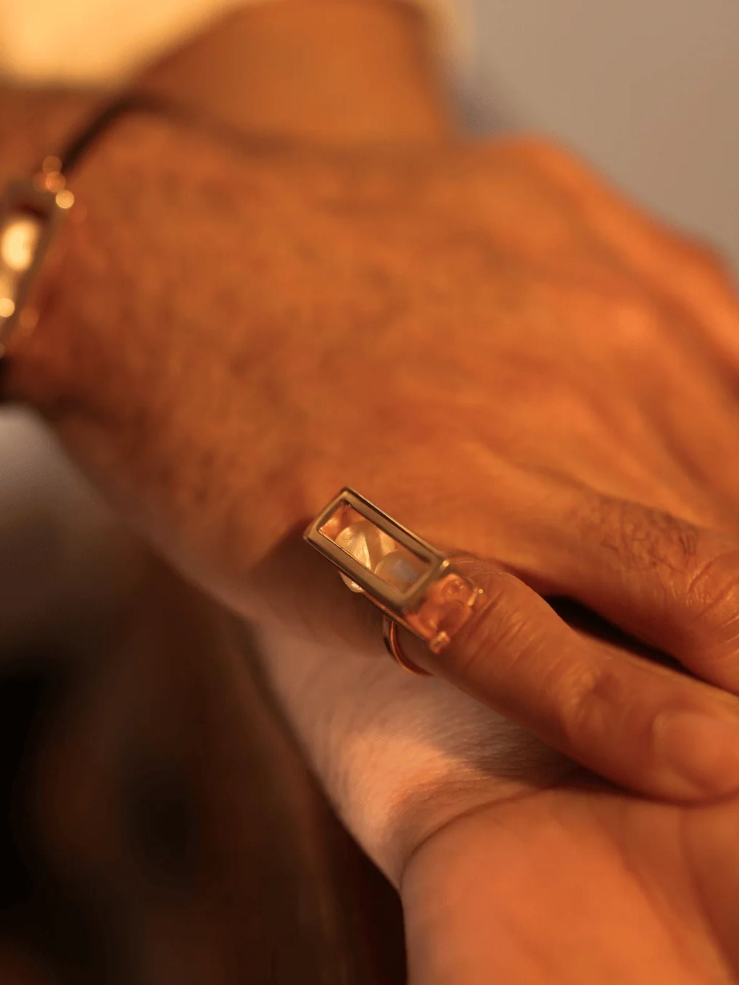 Close-up of large gold interchangeable box ring on model's hand, warm light