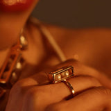 Close-up of model wearing large gold box ring with pearl beads, warm light