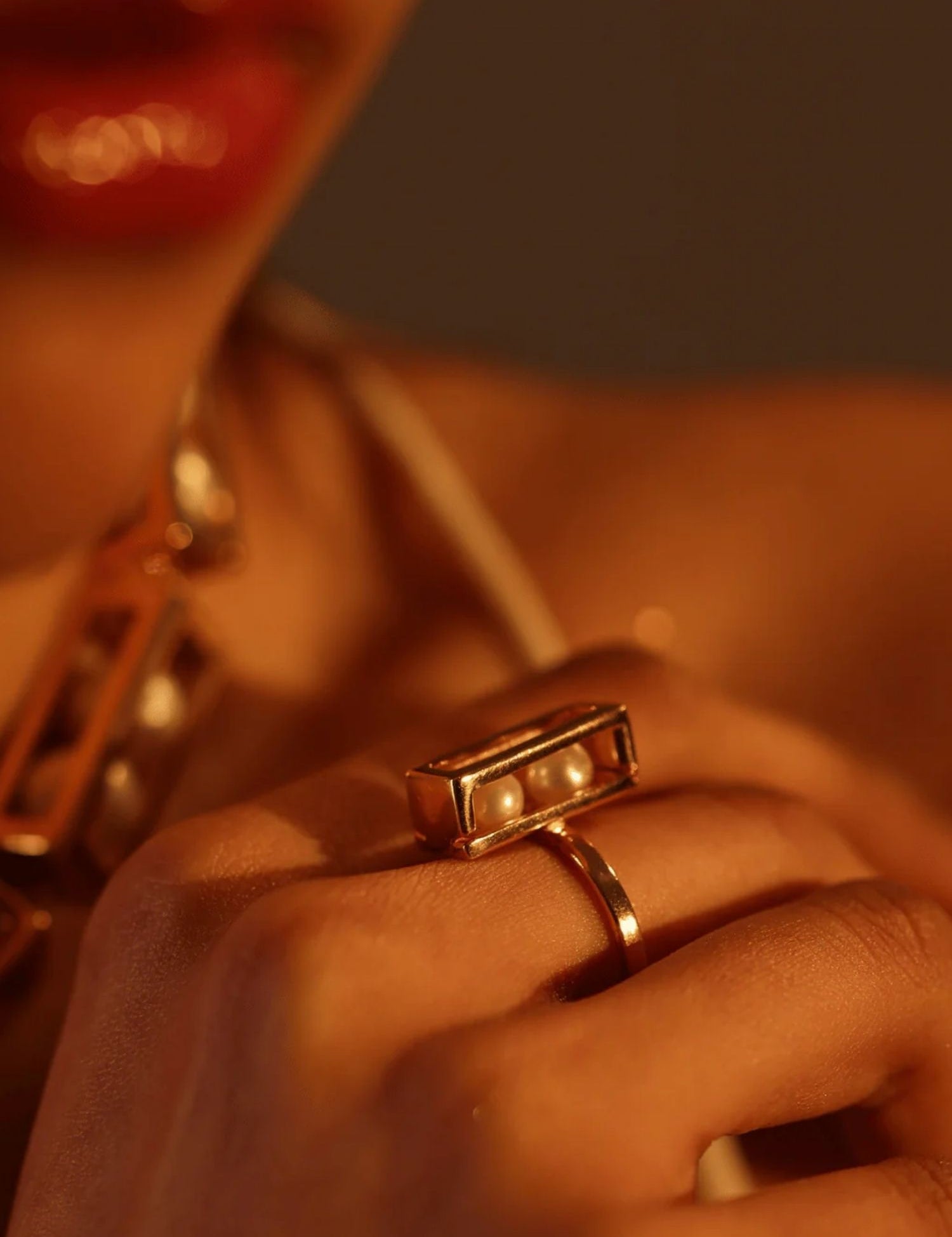 Close-up of model wearing large gold box ring with pearl beads, warm light