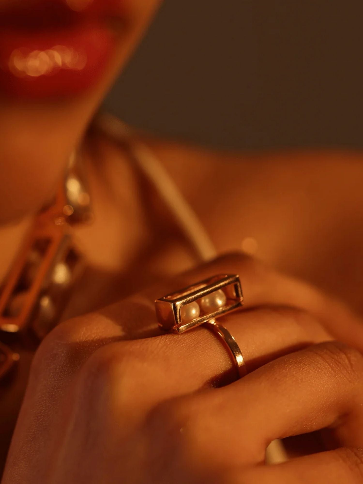 Close-up of model wearing large gold box ring with pearl beads, warm light