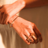Model wearing stacked gold interchangeable box rings, hands crossed at wrist