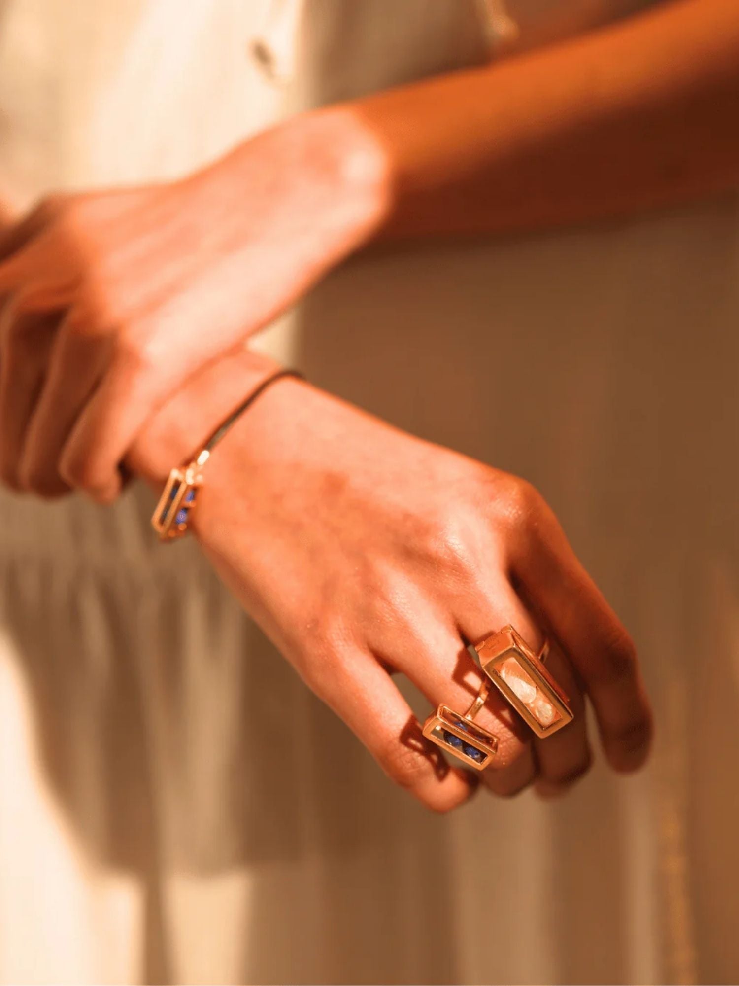 Model wearing stacked gold interchangeable box rings, hands crossed at wrist
