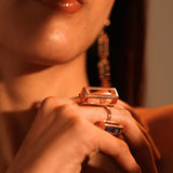 Model wearing two gold Fill Me In box rings stacked on hands, warm light
