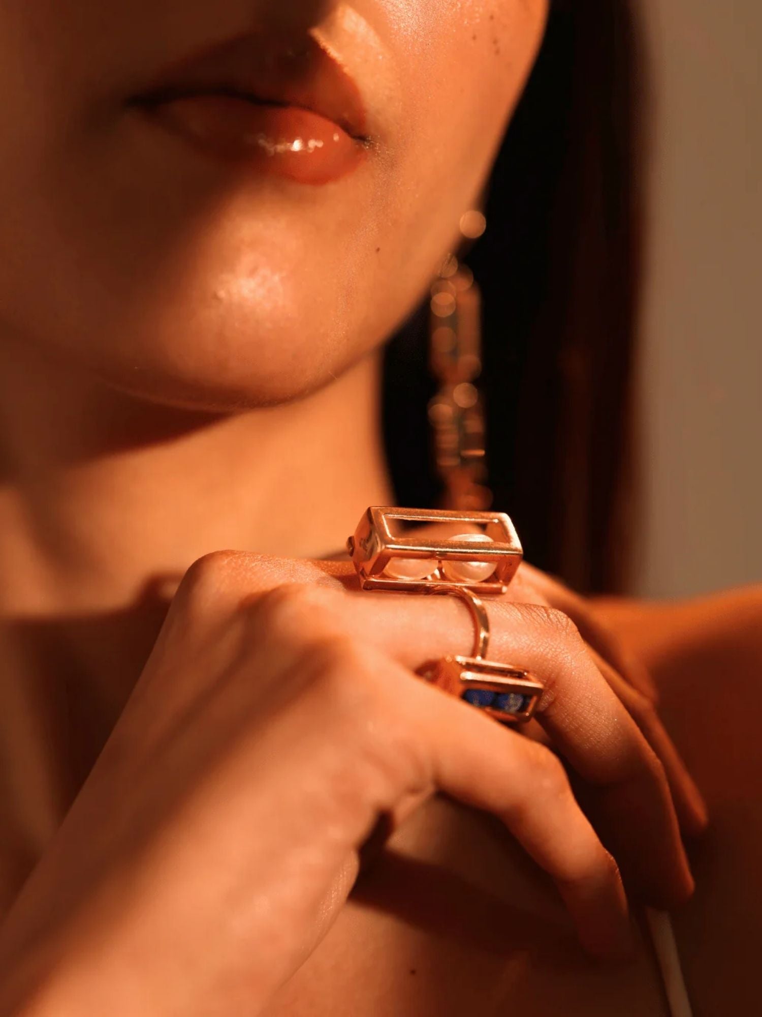 Model wearing two gold Fill Me In box rings stacked on hands, warm light