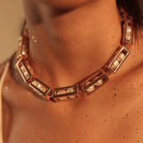 Model wearing large gold box link choker necklace with pearl beads, collarbone close-up