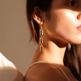 Model wearing long triple-drop gold box link earrings, side profile warm light