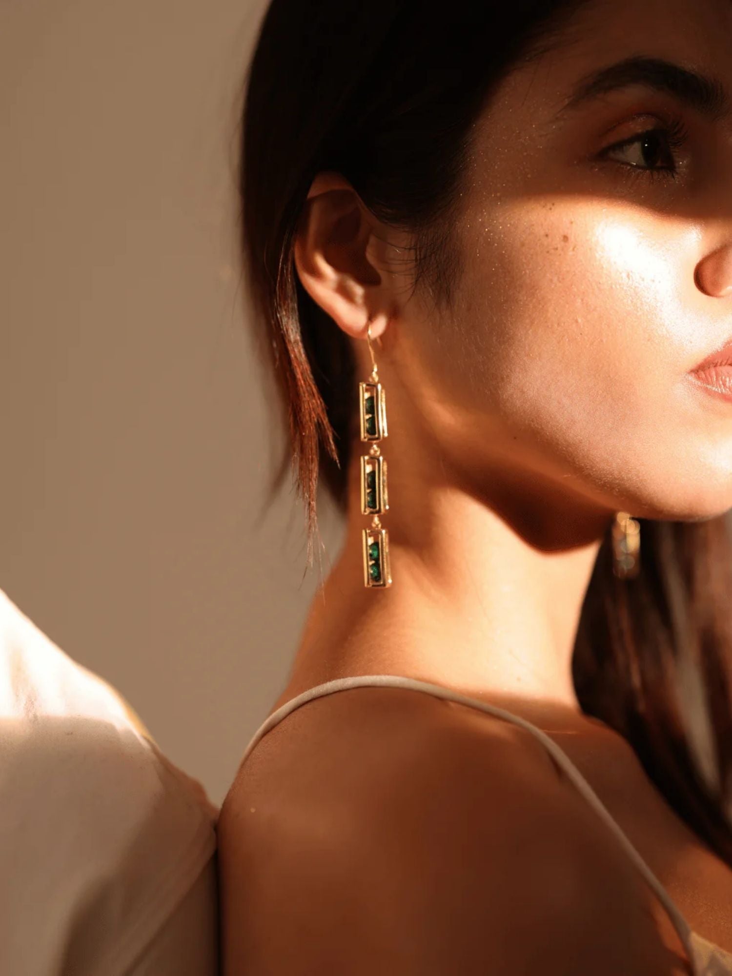 Model wearing long triple-drop gold box link earrings, side profile warm light