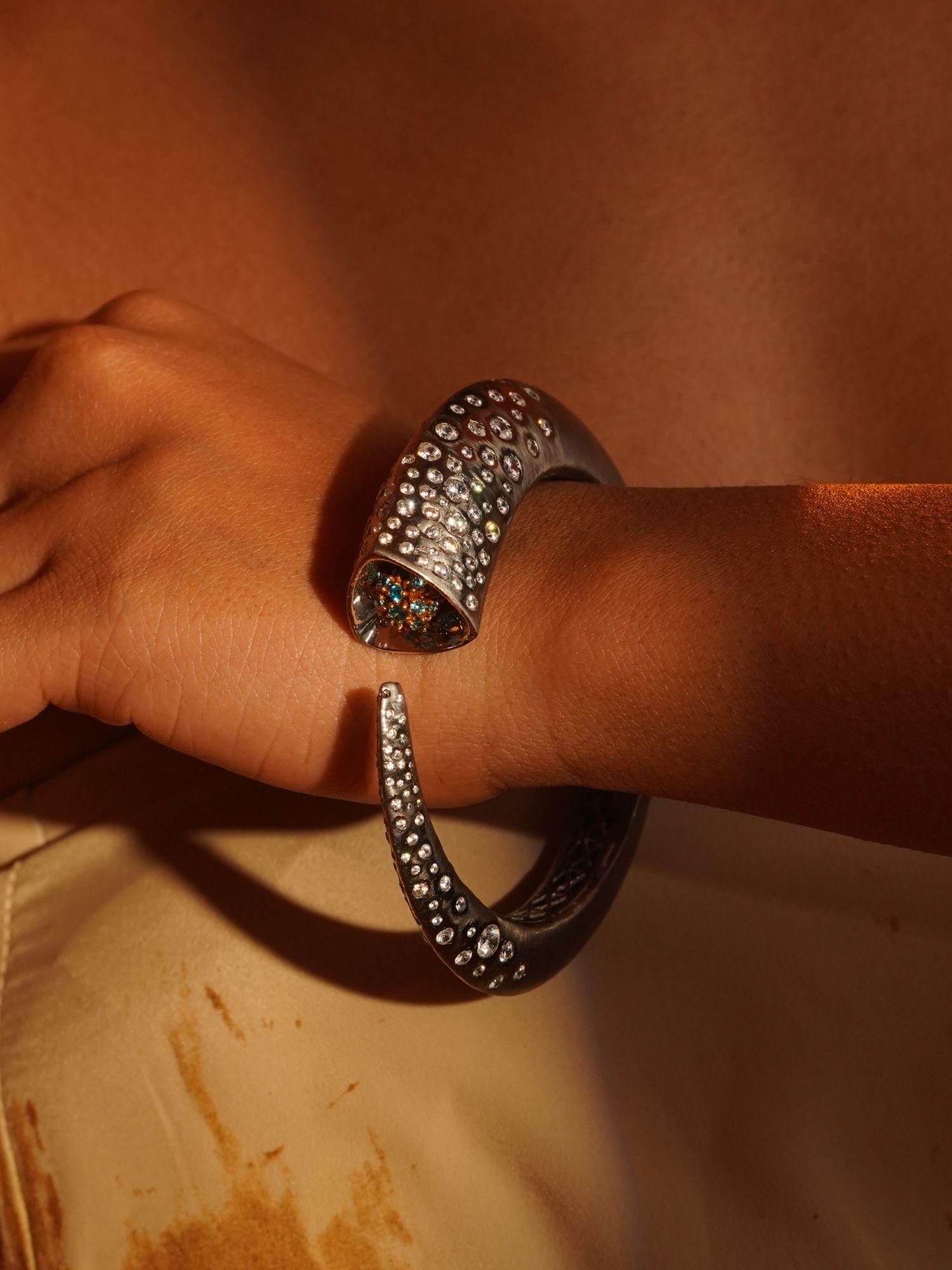 Irodori black oxidised silver bangle with zircon tip worn on wrist in warm close editorial shot.