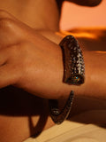Irodori black bangle on wrist with hands crossed in warm orange editorial light.