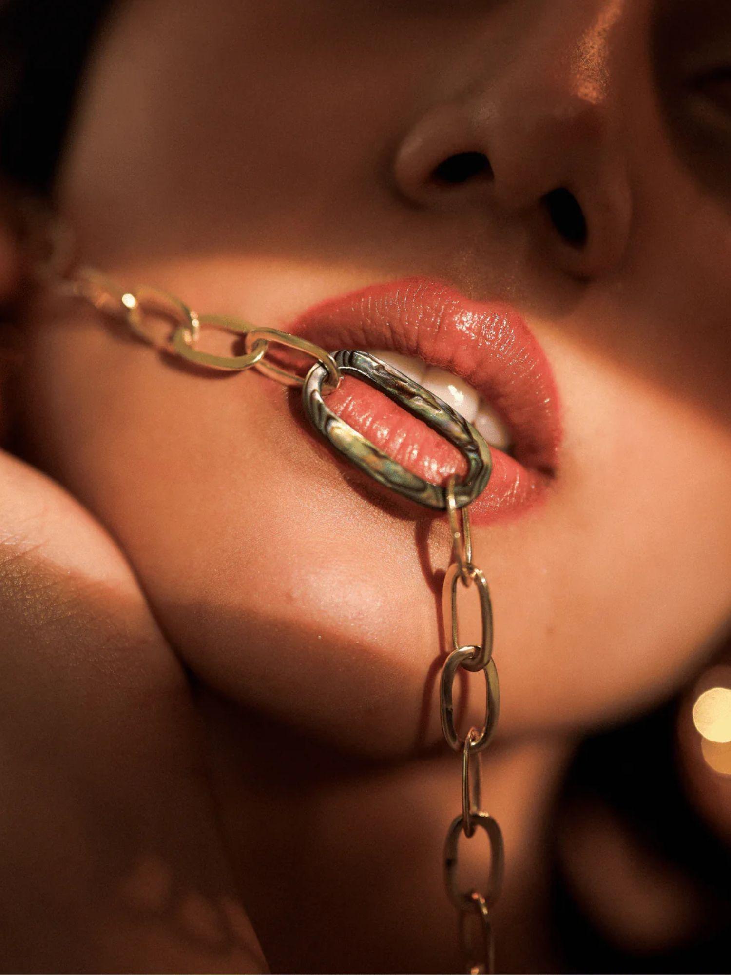 Model wearing gold abalone link chain necklace draped near mouth, close-up