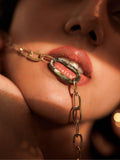 Model wearing gold abalone link chain necklace draped near mouth, close-up