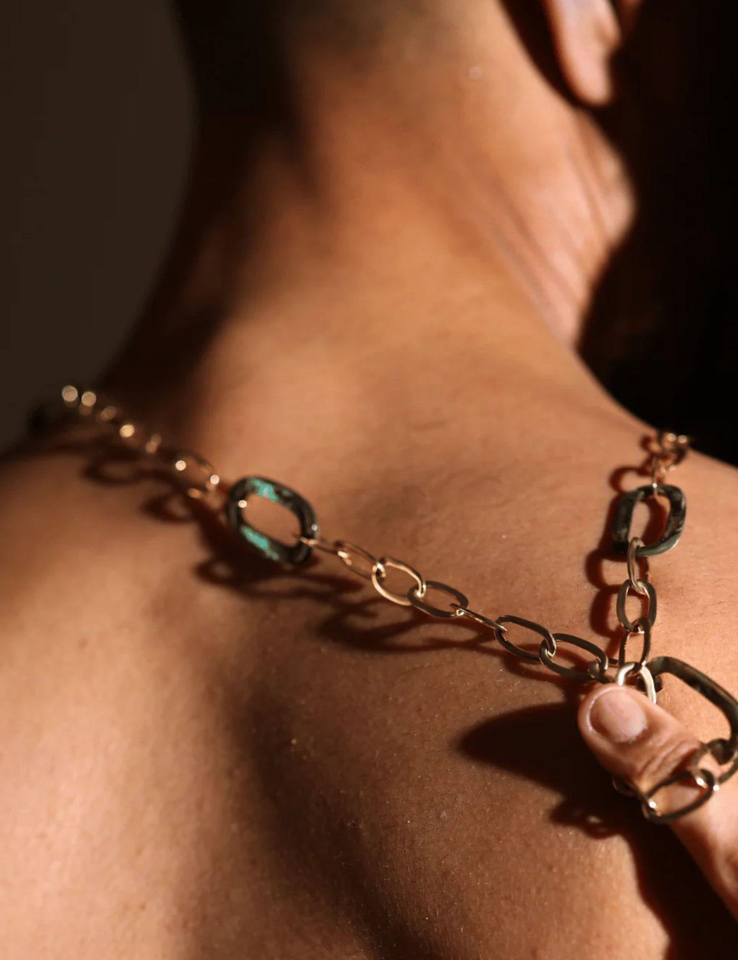 Gold abalone link chain worn on wrist as bracelet in warm dramatic lighting