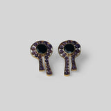 Kōmon keyhole stud earrings with black spinel centre and amethyst border in gold on neutral background.